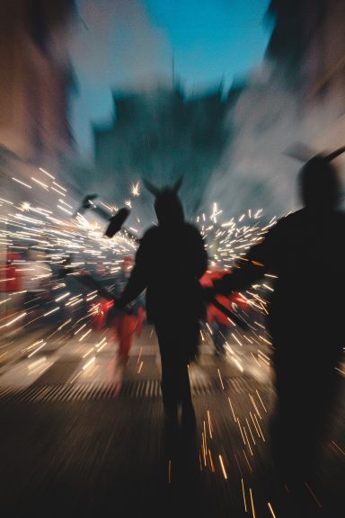 Personas con cuernos y pirotecnia en un festival, con un fondo borroso.
