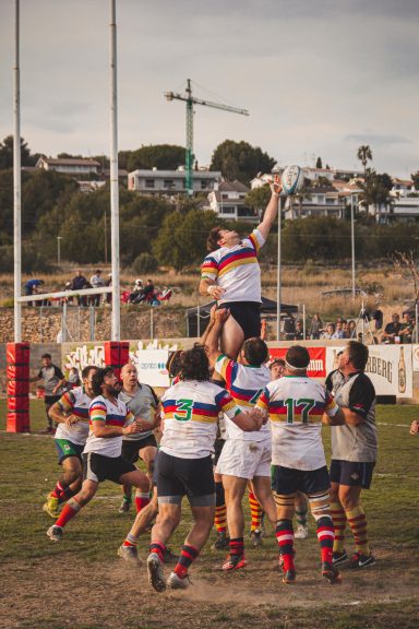 Jugadores de rugby levantan a un compañero en un saque de banda en un campo al aire libre.