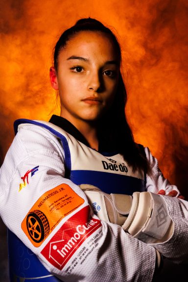 Joven atleta de taekwondo con vestimenta deportiva y fondo anaranjado.